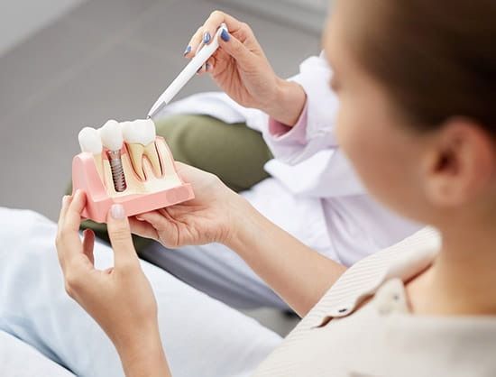 Dentist pointing at a tooth model to explain dental implant procedure to a patient.