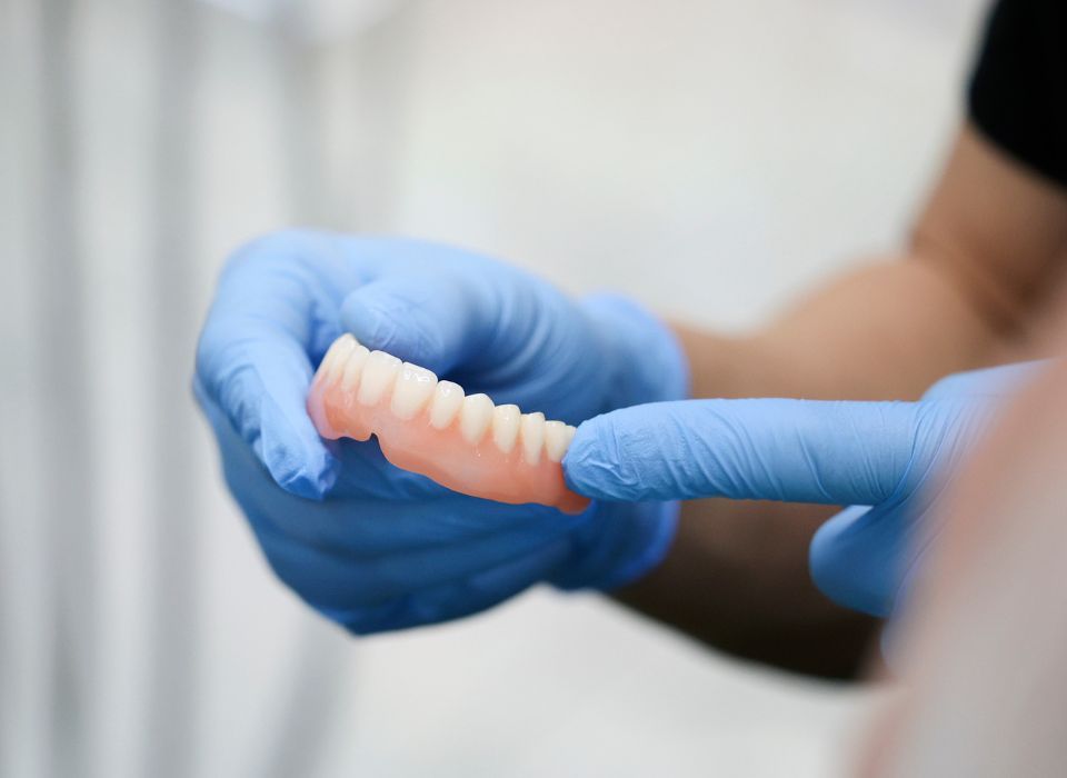 Hands in blue gloves holding a set of dentures.