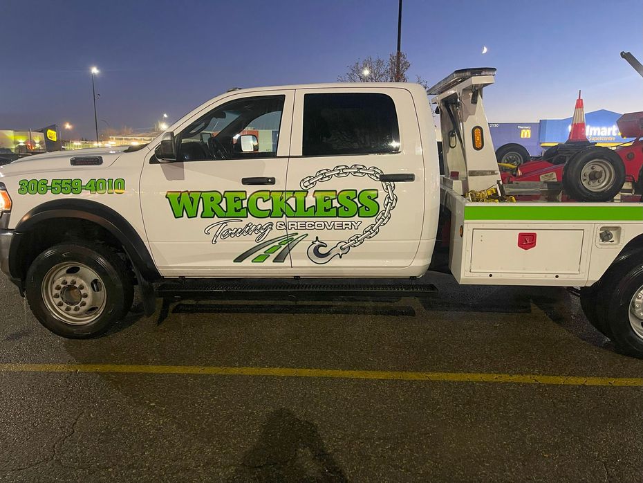 White tow truck with green “WRECKLESS” lettering parked in a lot at dusk.