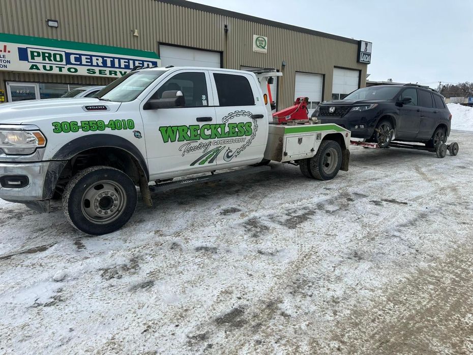 White tow truck hauling a black SUV in a snowy parking lot outside a garage