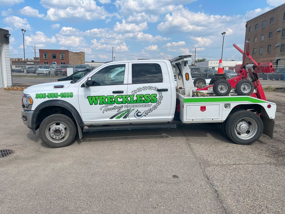 White wrecking tow truck with red equipment parked in a lot under a cloudy sky