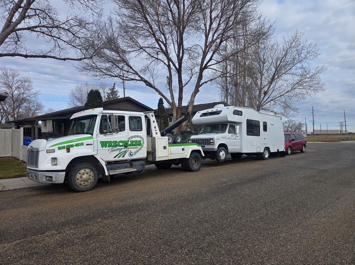 Tow truck towing a white RV on a residential street under cloudy skies