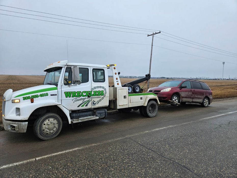 Tow truck towing a maroon SUV on a wet rural roadside under cloudy skies