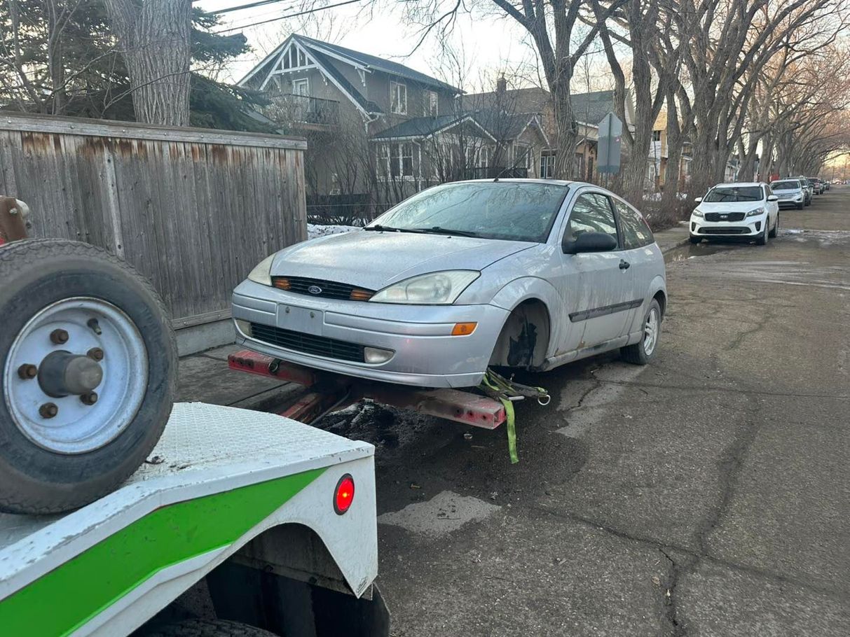 Silver sedan on a tow trailer in a residential street, with another car parked behind.