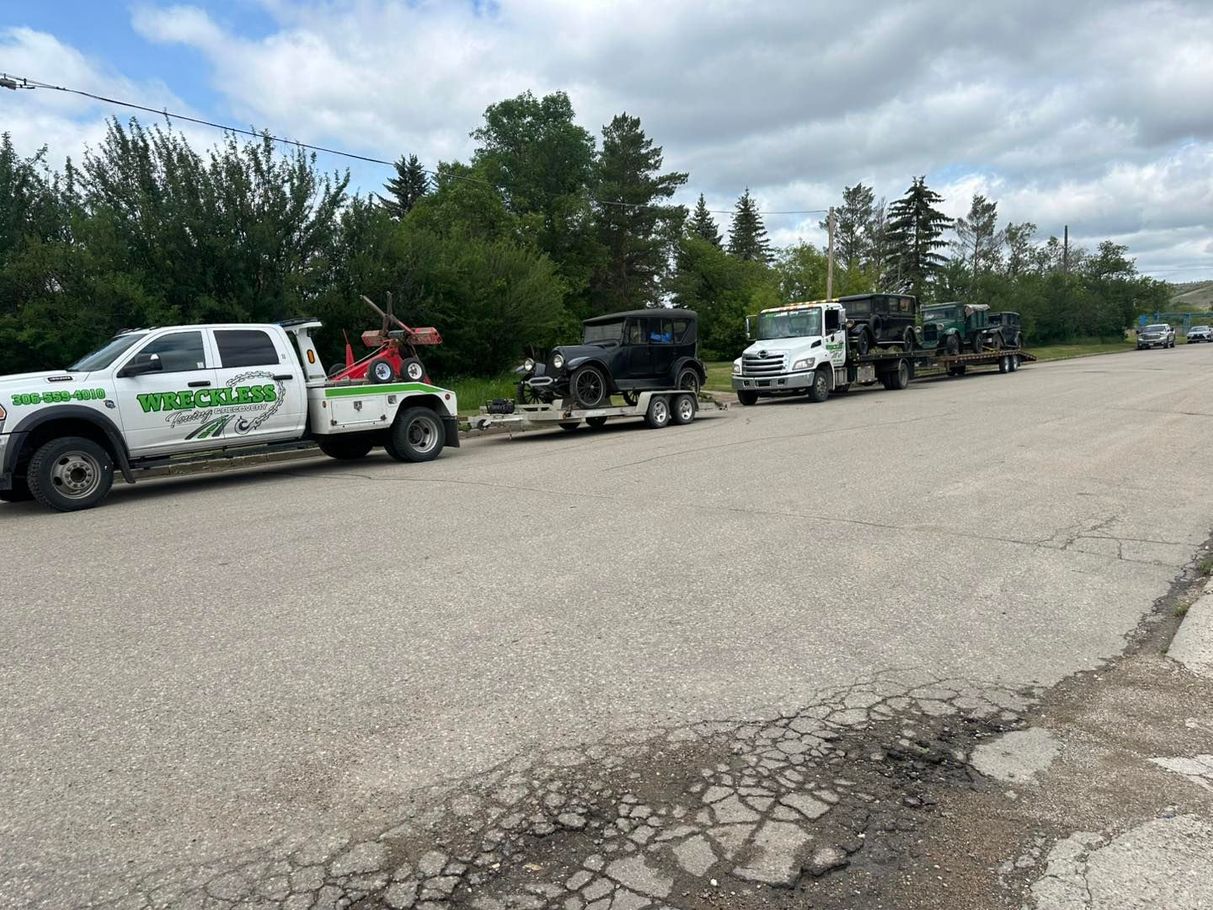 Three tow trucks lined up on a cracked road beside trees under a cloudy sky