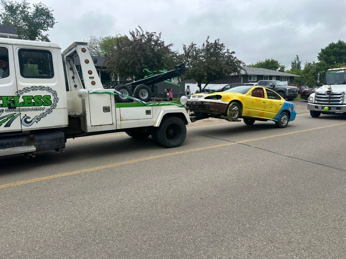 Tow truck lifting a yellow sedan after a roadside crash, with damaged vehicles on a street