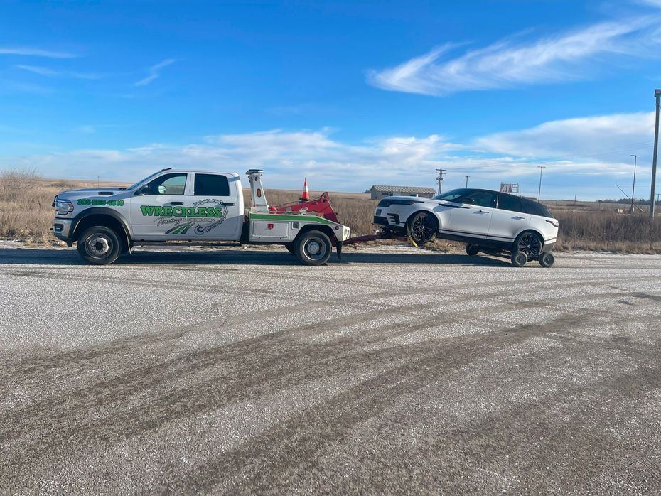 Tow truck towing a white SUV on a gravel road under a blue sky