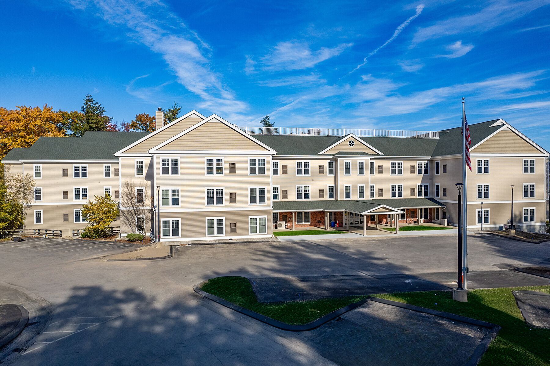 Multi-story tan building with a central covered porch and a flagpole on a sunny day.