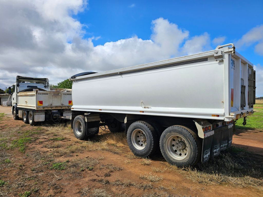 A white dump truck with a trailer attached to it is parked in a dirt field.