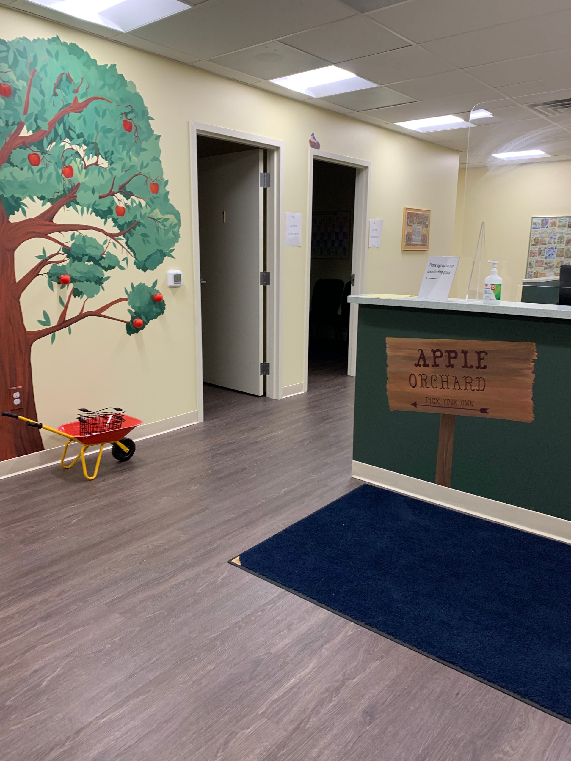 A room with a wheelbarrow and a painting of an apple tree on the wall at Advocare Fairmount Pediatrics
