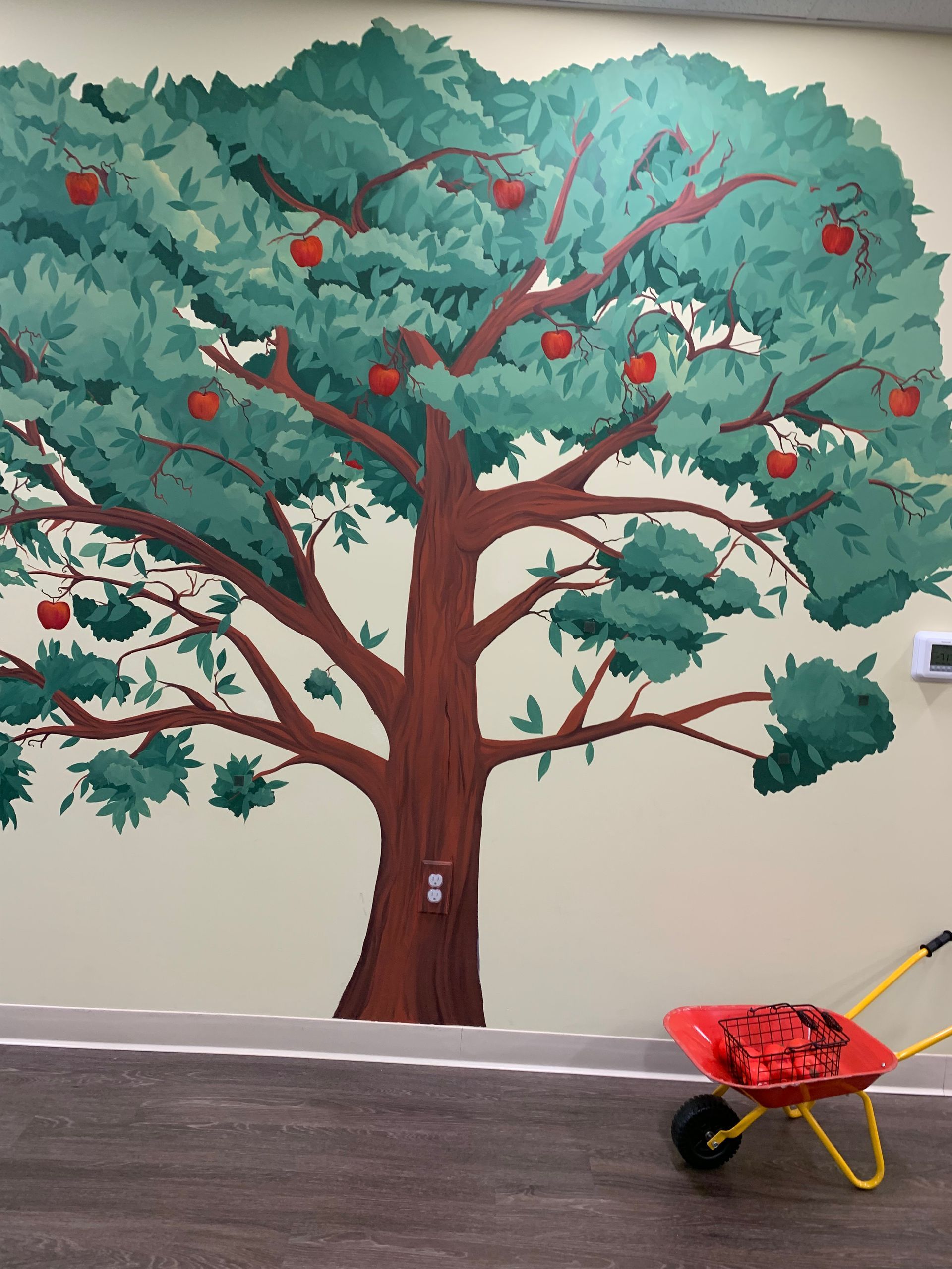 A wheelbarrow sits in front of a painting of an apple tree at Advocare Fairmount Pediatrics