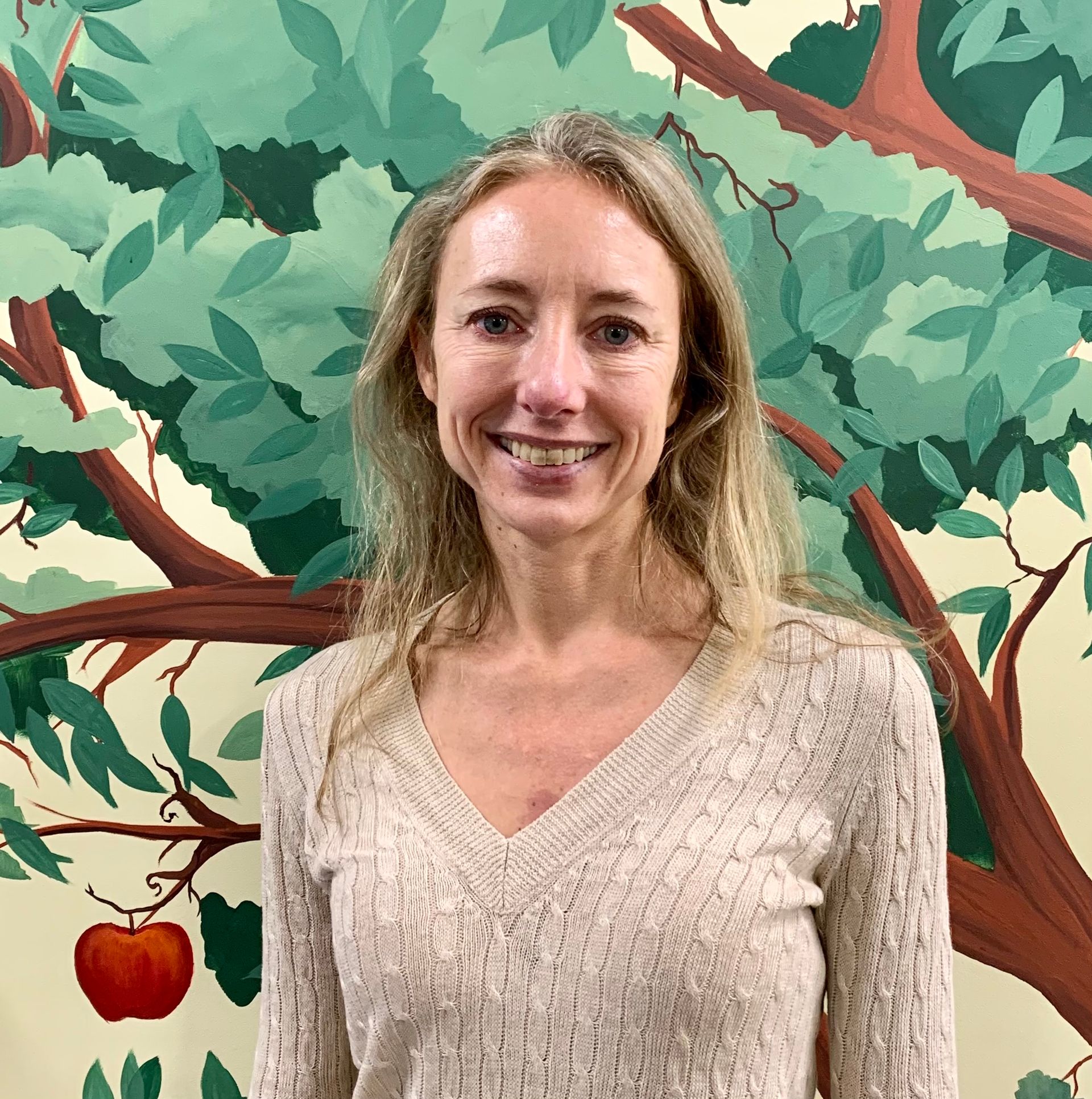 A woman is smiling in front of a painting of an apple tree at Advocare Fairmount Pediatrics