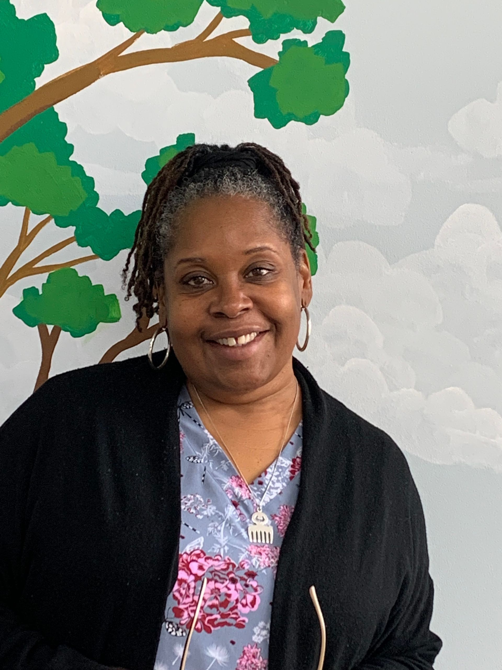 A nurse at Advocare Fairmount Pediatrics is smiling in front of a painting of trees on a wall.