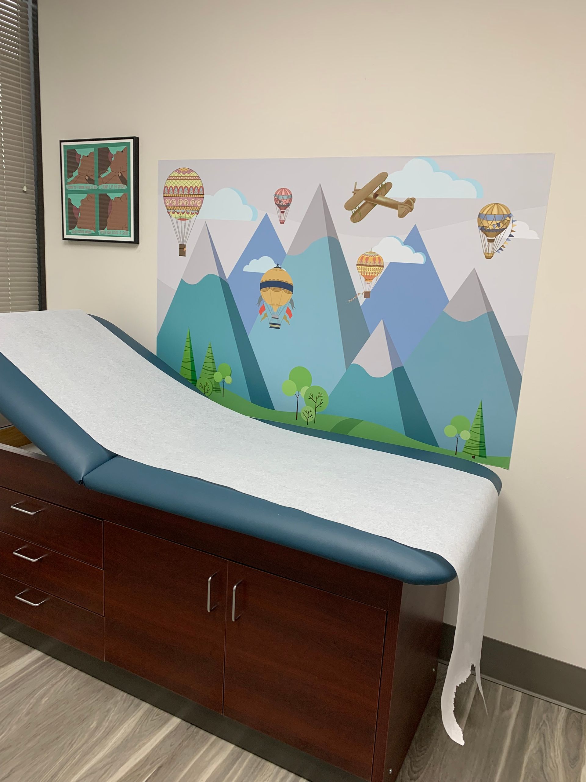 A doctor 's office with a painting of hot air balloons and mountains on the wall at at Advocare Fairmount Pediatrics