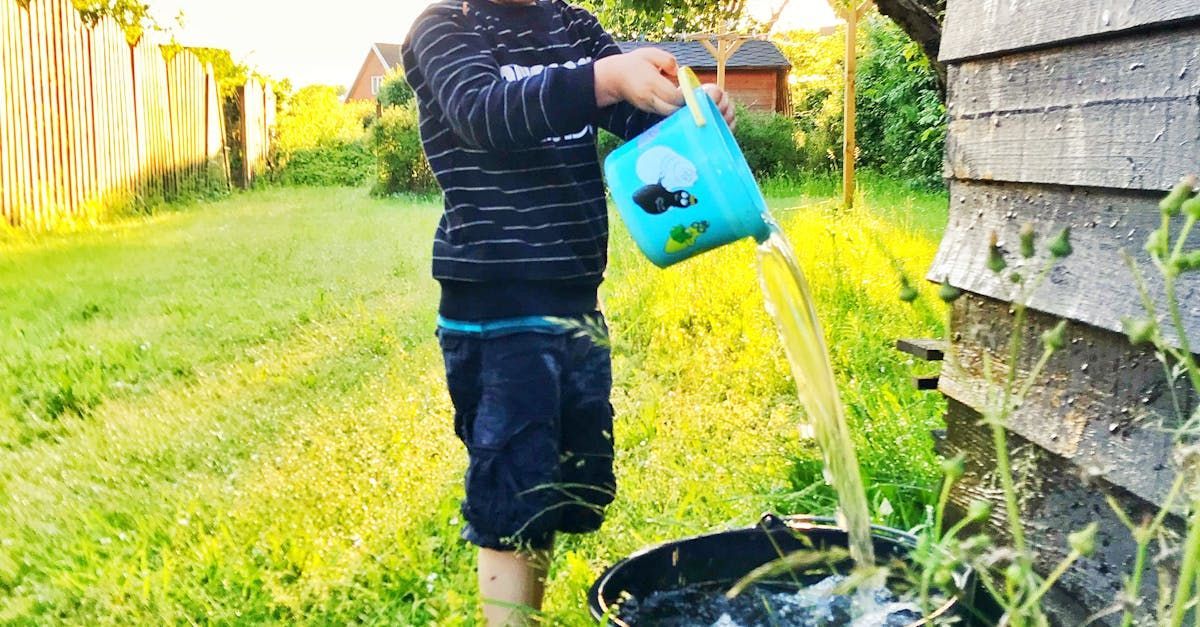 A young boy is pouring water from a watering can into a bucket. Eliminate standing water!