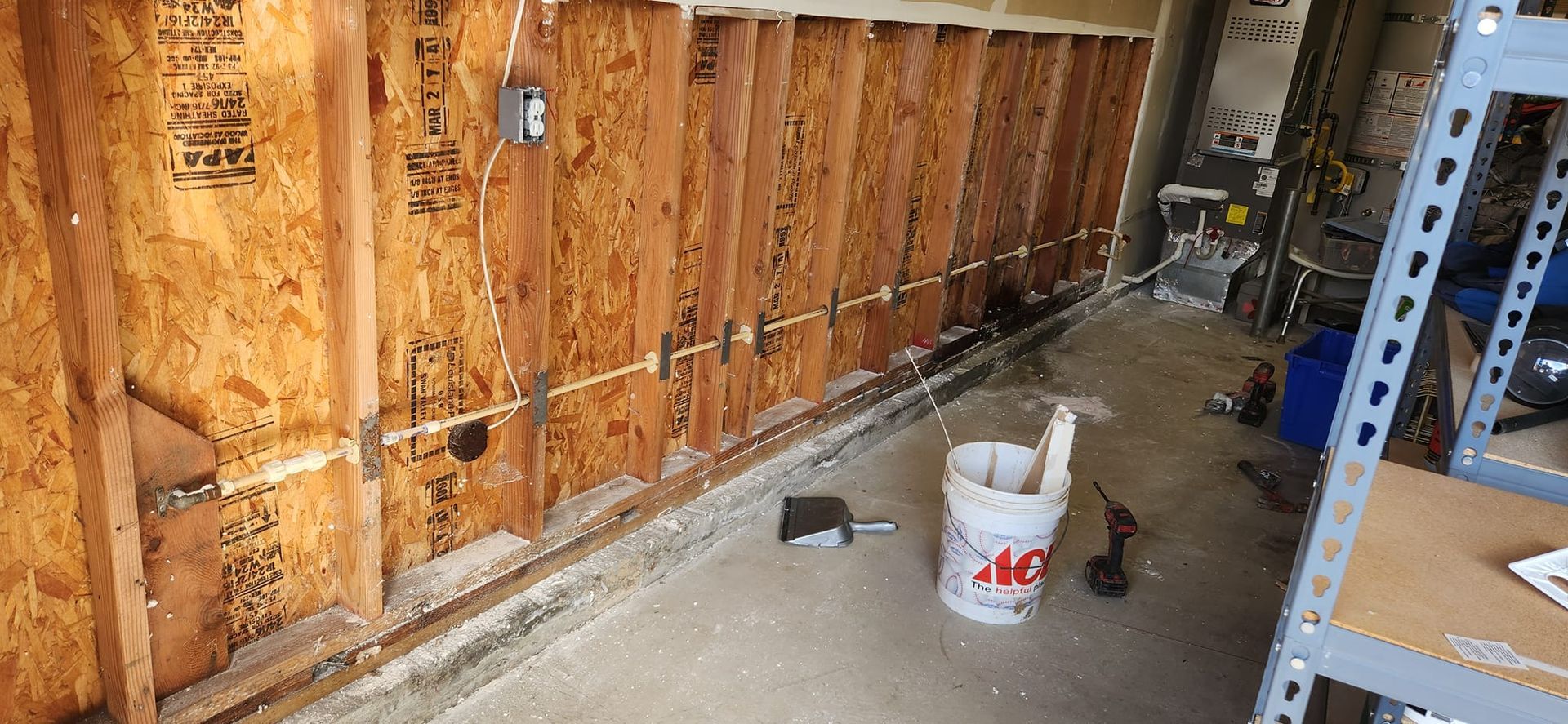 A partially finished garage wall with exposed wood studs, electrical wiring secured with metal straps, and a paint bucket.