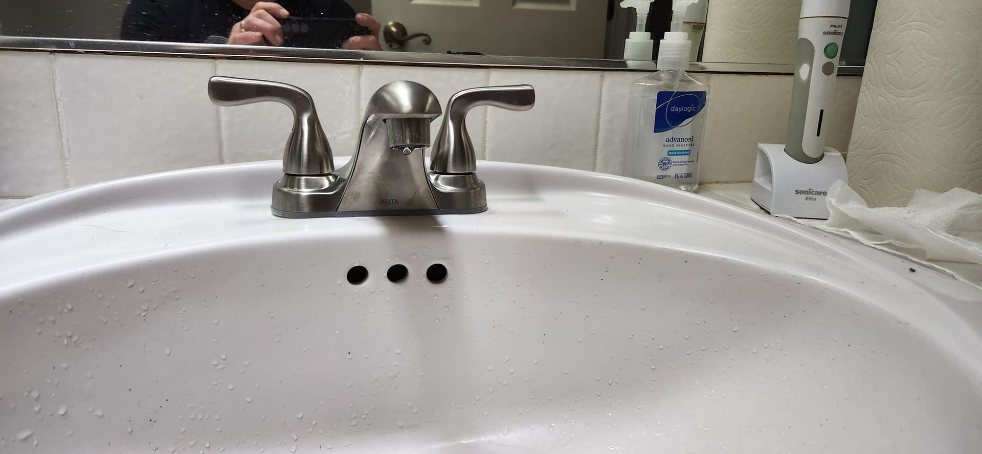A brushed nickel bathroom faucet centered above a white sink with a visible overflow drain and a bathroom vanity mirror.