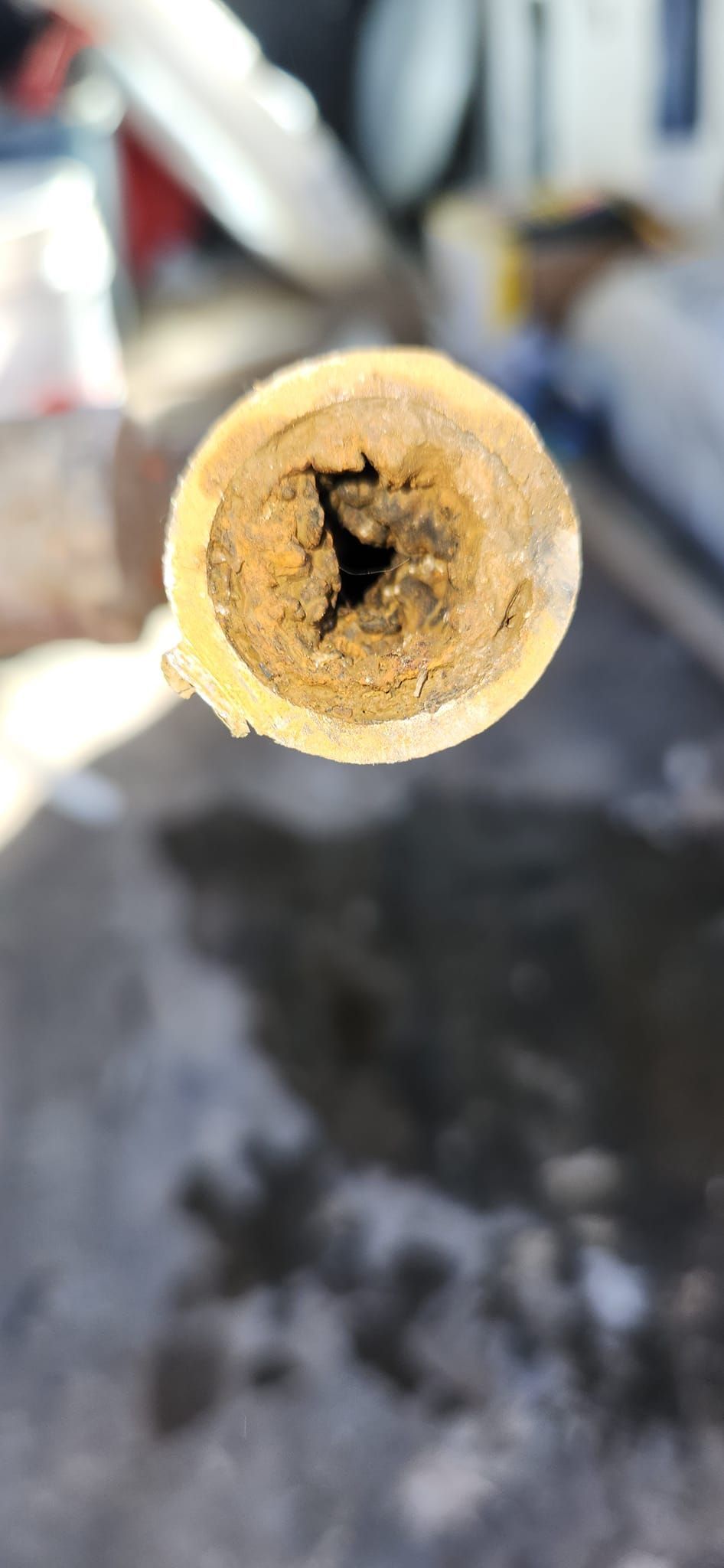 A close-up view of a metal pipe cross-section heavily clogged with thick, yellowish-brown mineral scale and rust deposits.