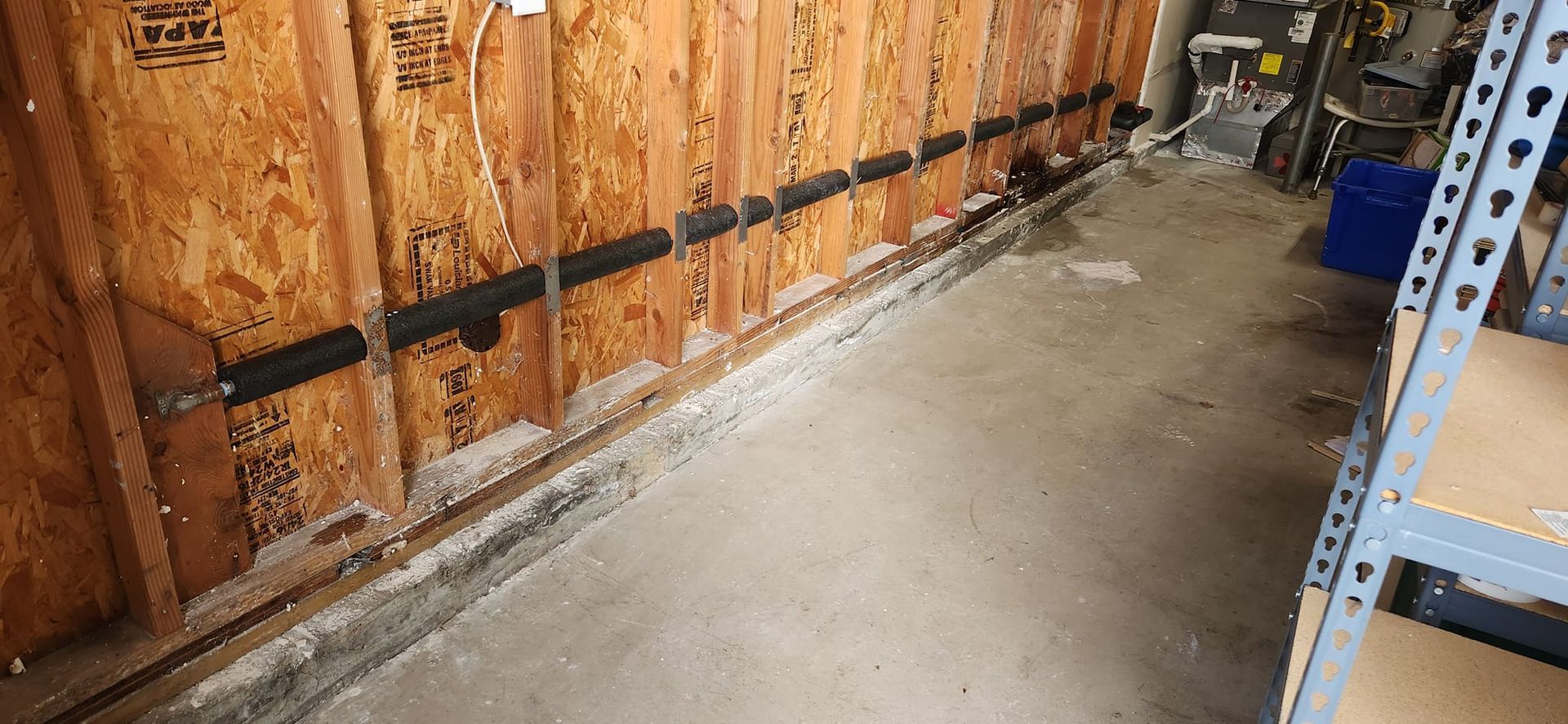 A black pipe runs horizontally along a wood-paneled wall above a concrete garage floor.