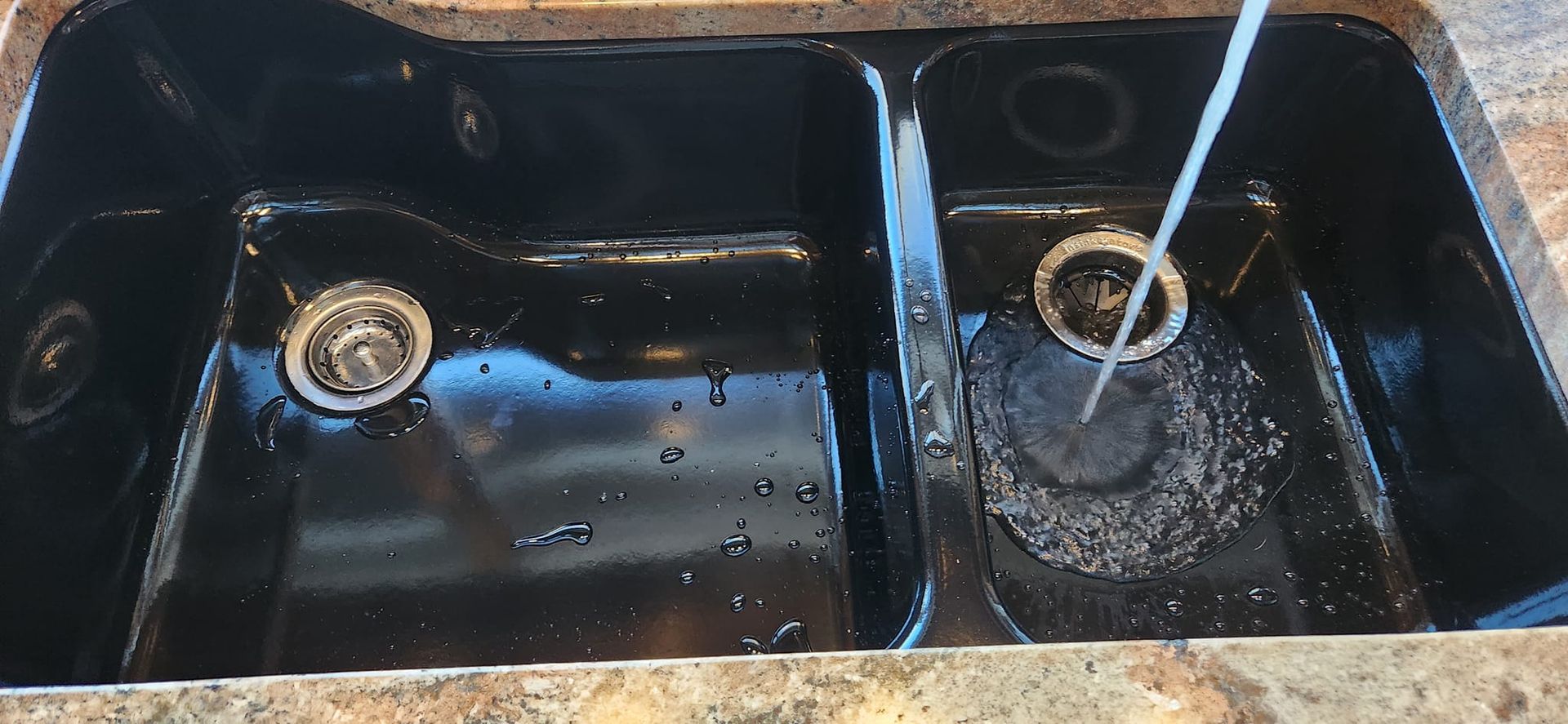 A two-basin black kitchen sink with a water faucet running into the smaller right-hand basin.