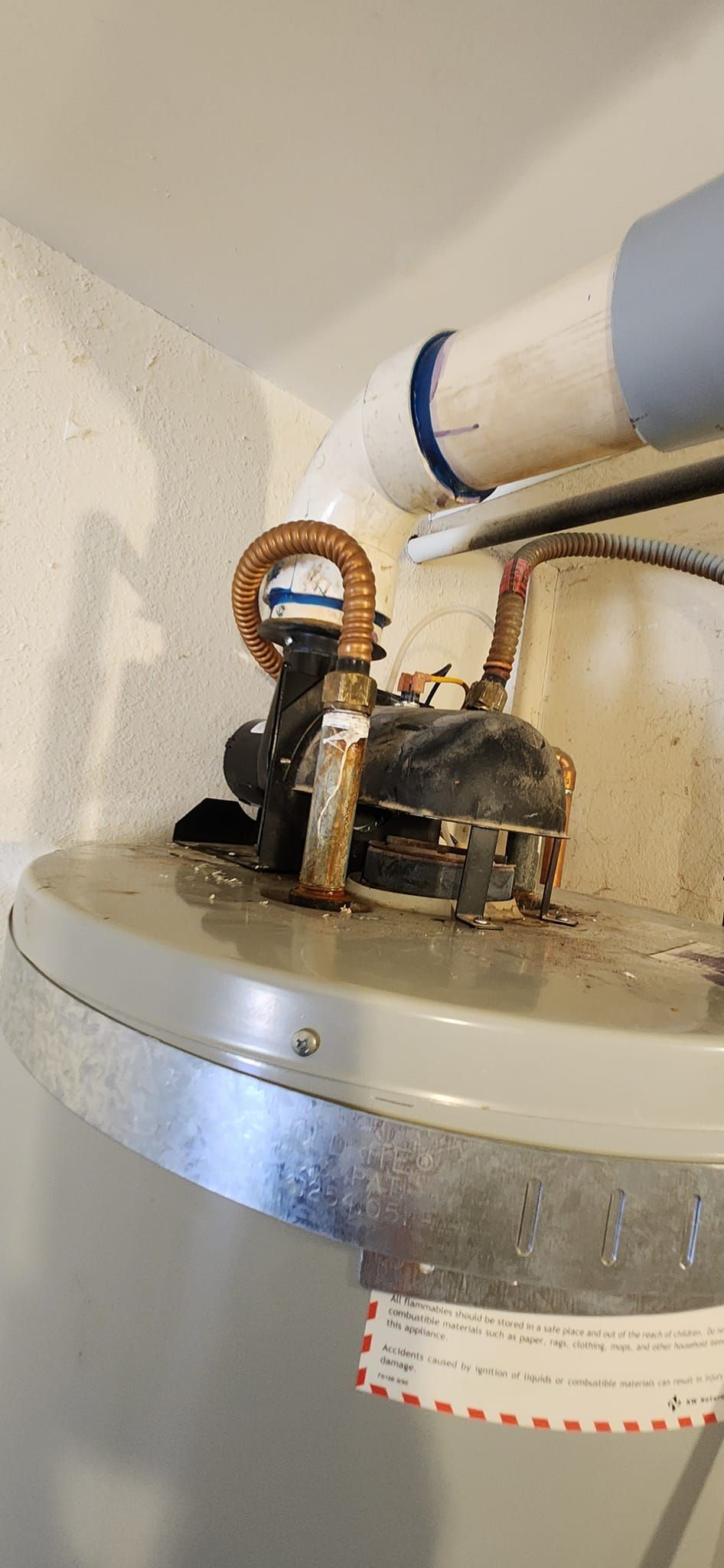 Top of a residential water heater showing corroded pipe connections, insulation, and a vent pipe.