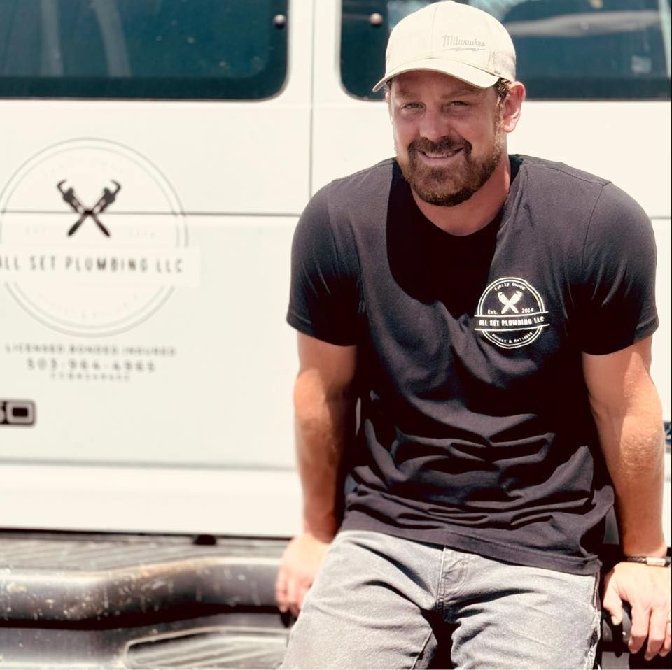 A man in a black t-shirt and cap smiling in front of a white work van with 