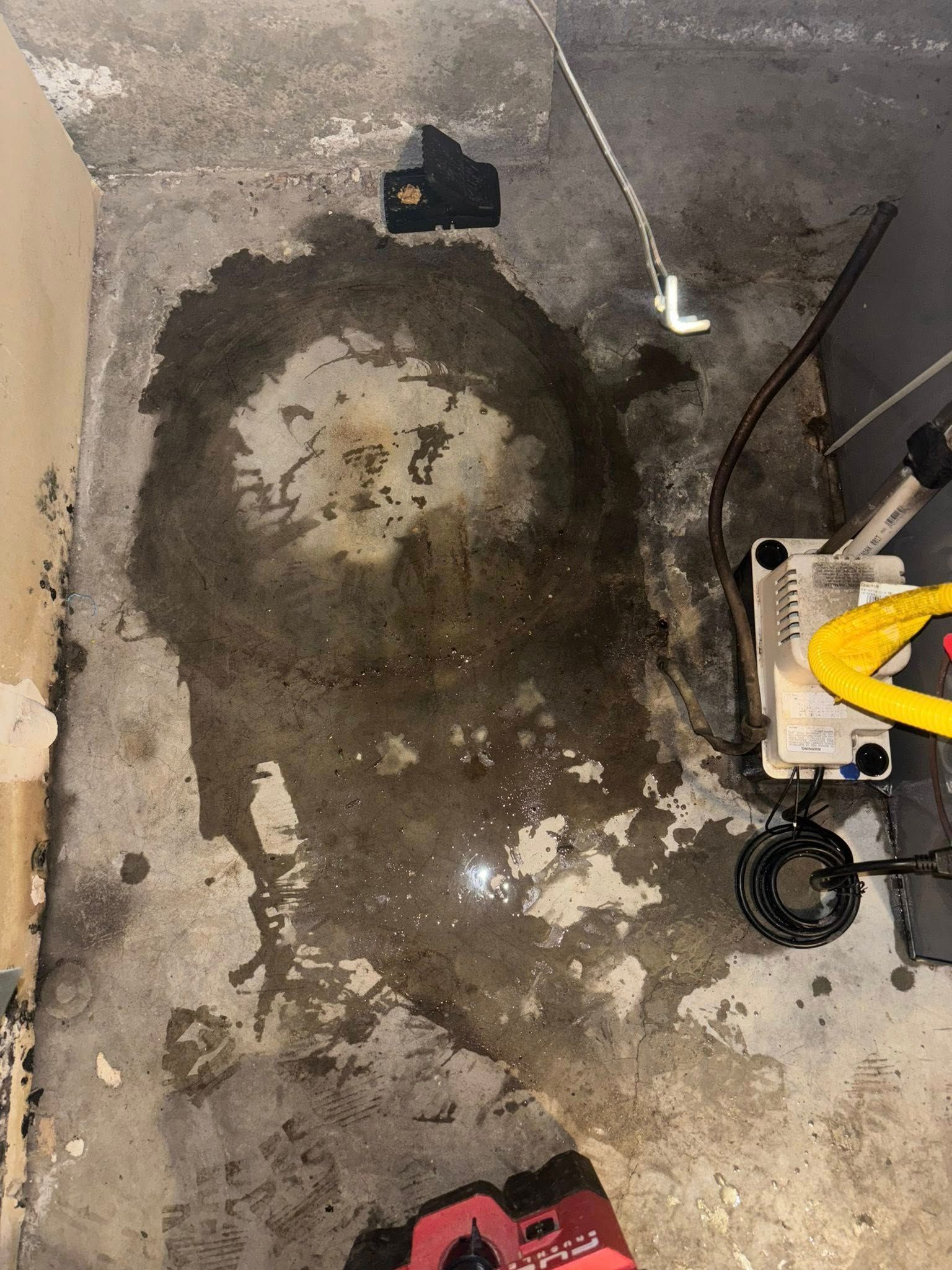 A large, dark wet spot on a gray concrete floor next to a condensate pump and white tubing.