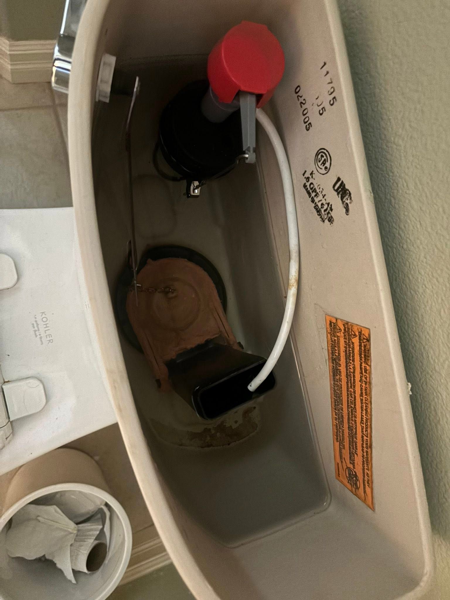 The interior of an open toilet tank, showing a red-capped fill valve and a black flapper connected to the flush lever.