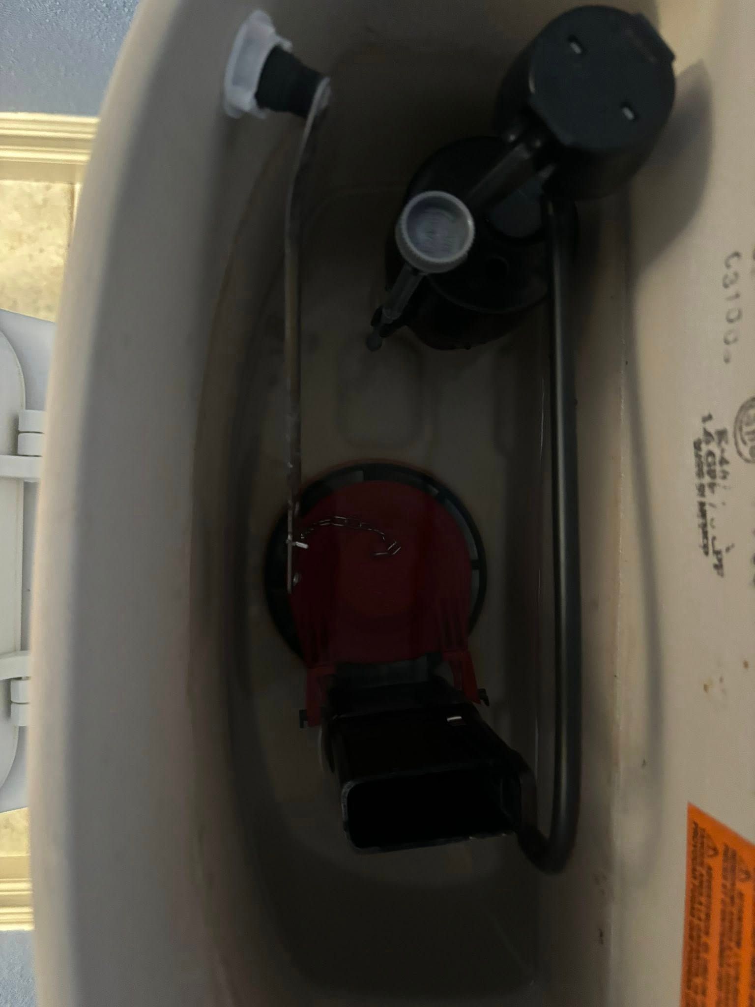 Inside view of a toilet tank showing the internal flushing mechanism, fill valve, and red canister flush valve.