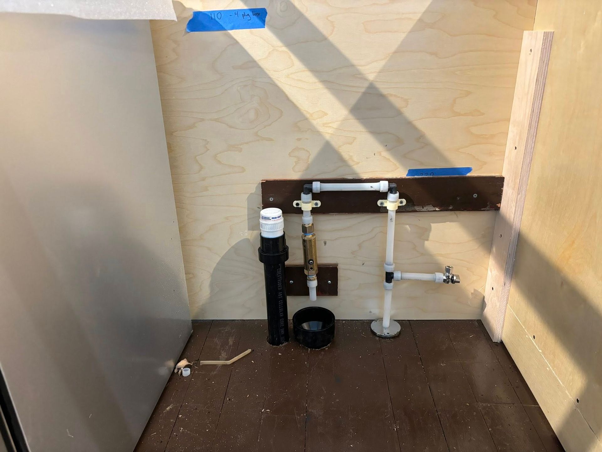 Plumbing setup with PEX pipes, a shut-off valve, and a drain pipe on a plywood wall in a workspace.