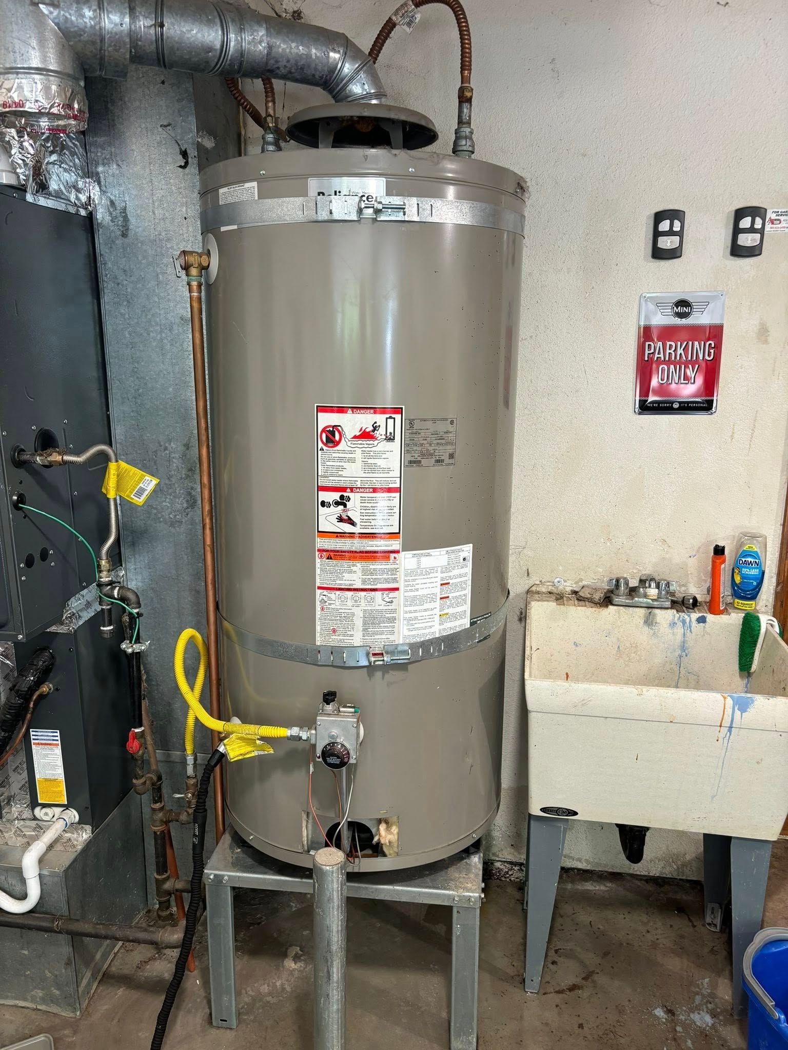 A gas water heater stands on a metal platform next to a utility sink in a residential basement.