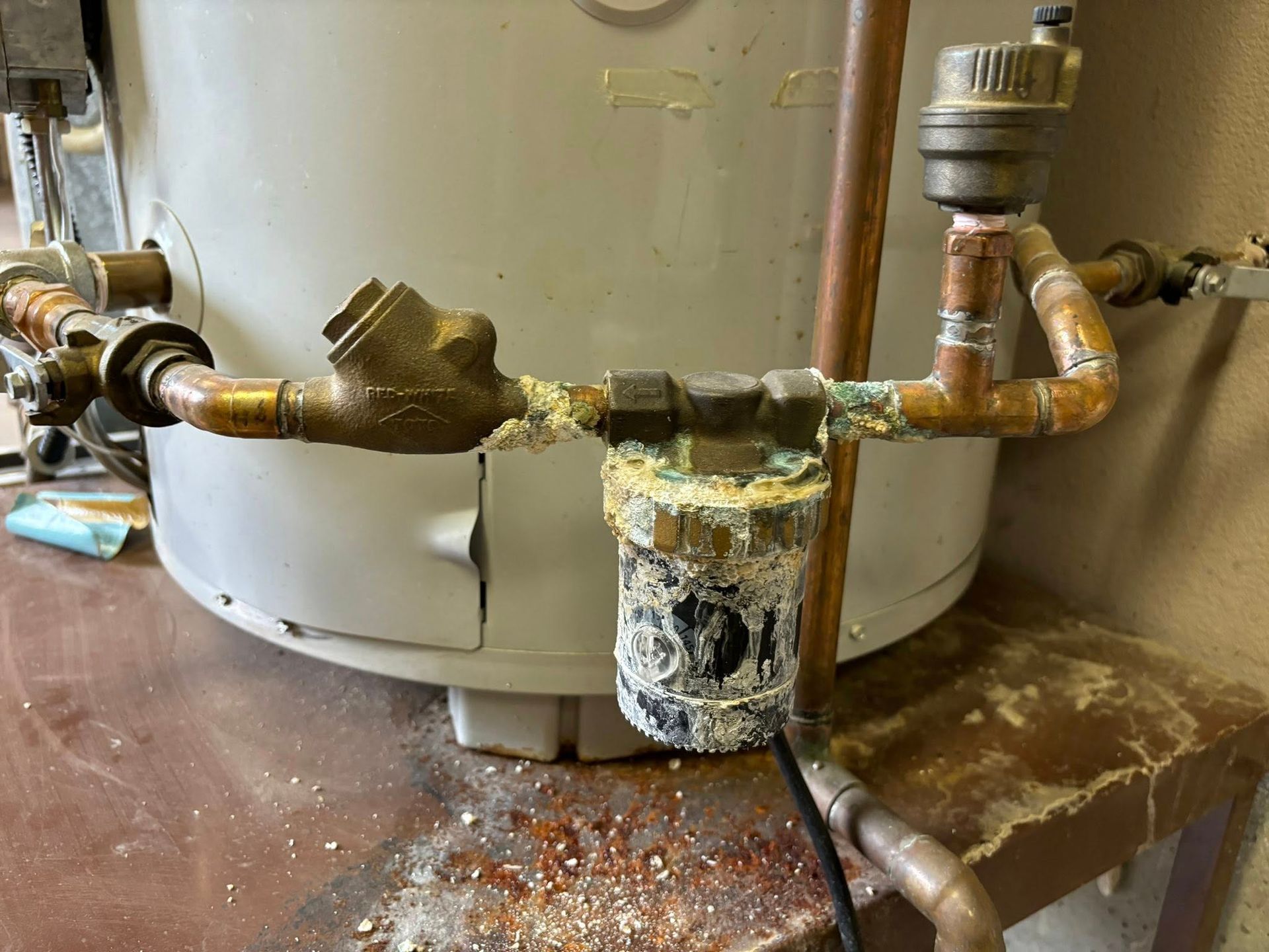 Corroded plumbing components and a mineral-encrusted water filter housing attached to a residential water heater.