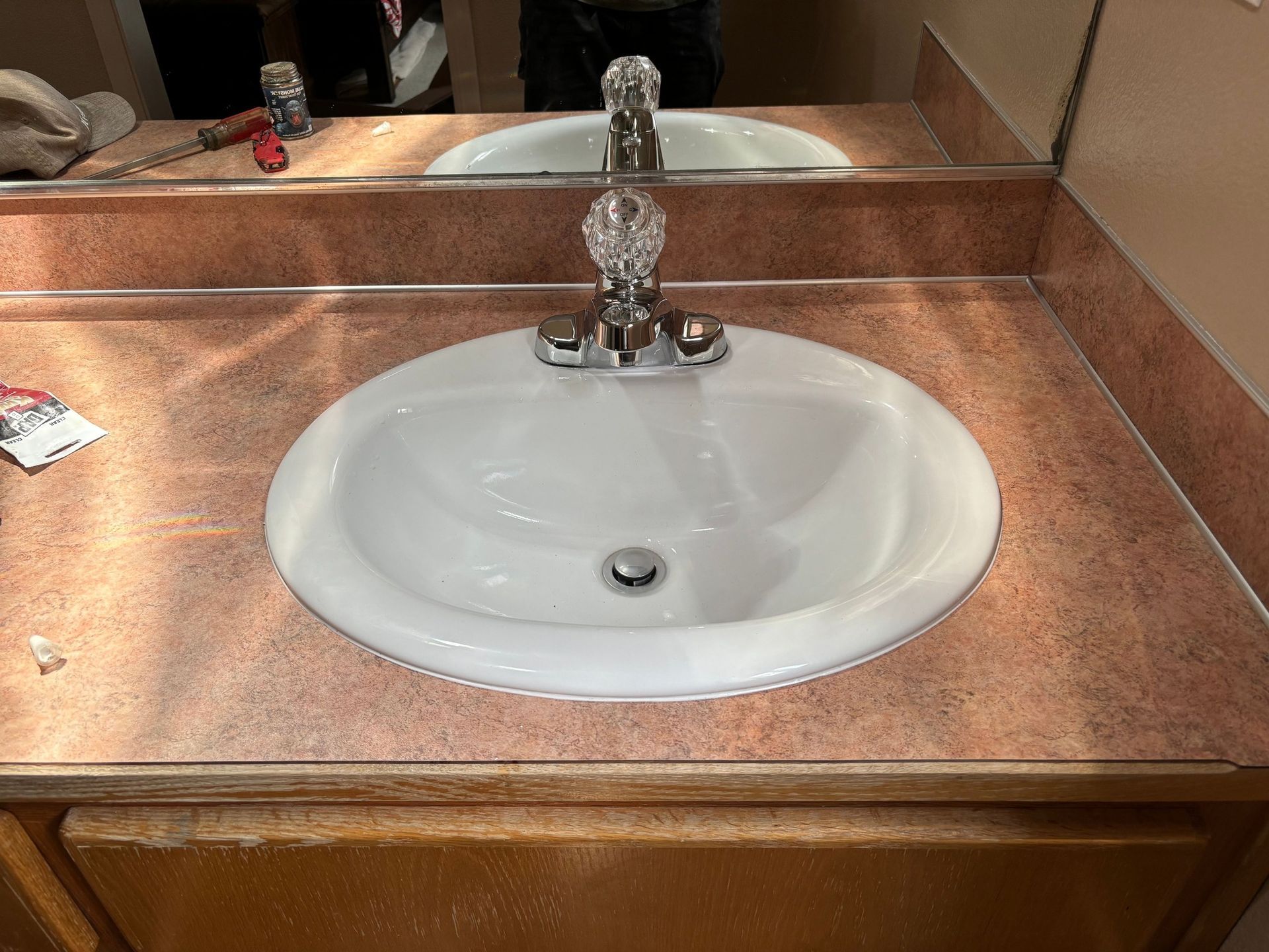 A white drop-in bathroom sink with a crystal-knob faucet set into a reddish-brown, speckled laminate countertop.