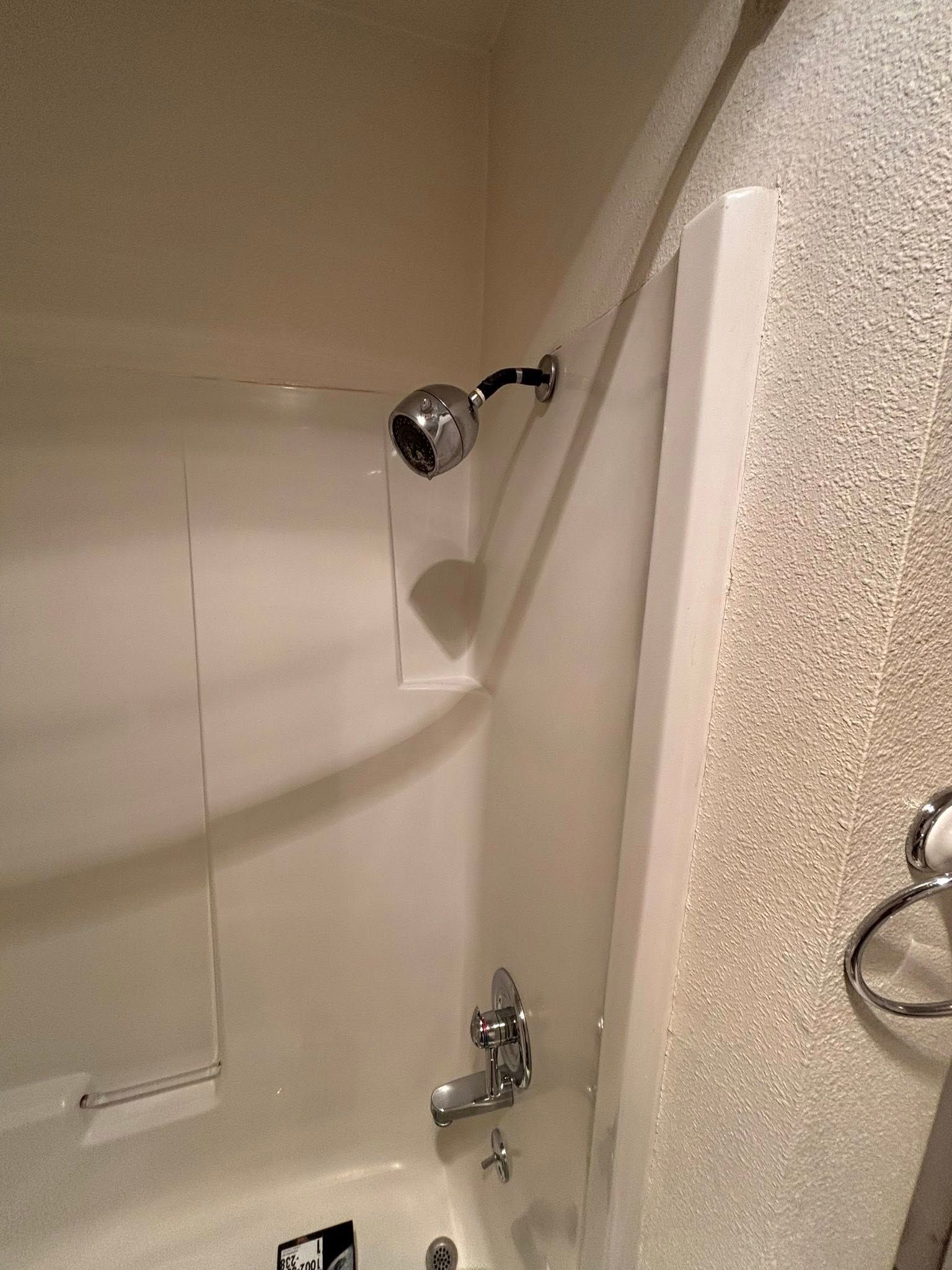 A white fiberglass shower stall featuring a chrome shower head, faucet, and mixer handle against a textured beige wall.