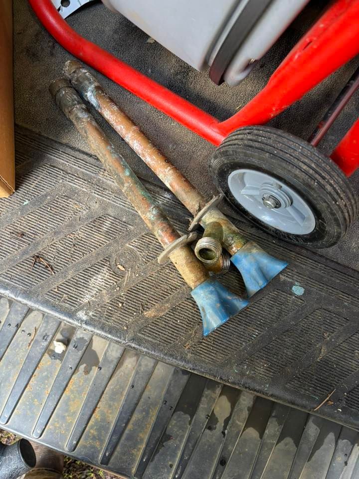 Two old copper pipes with blue-taped ends lie on a textured black rubber mat next to a red metal equipment cart wheel.
