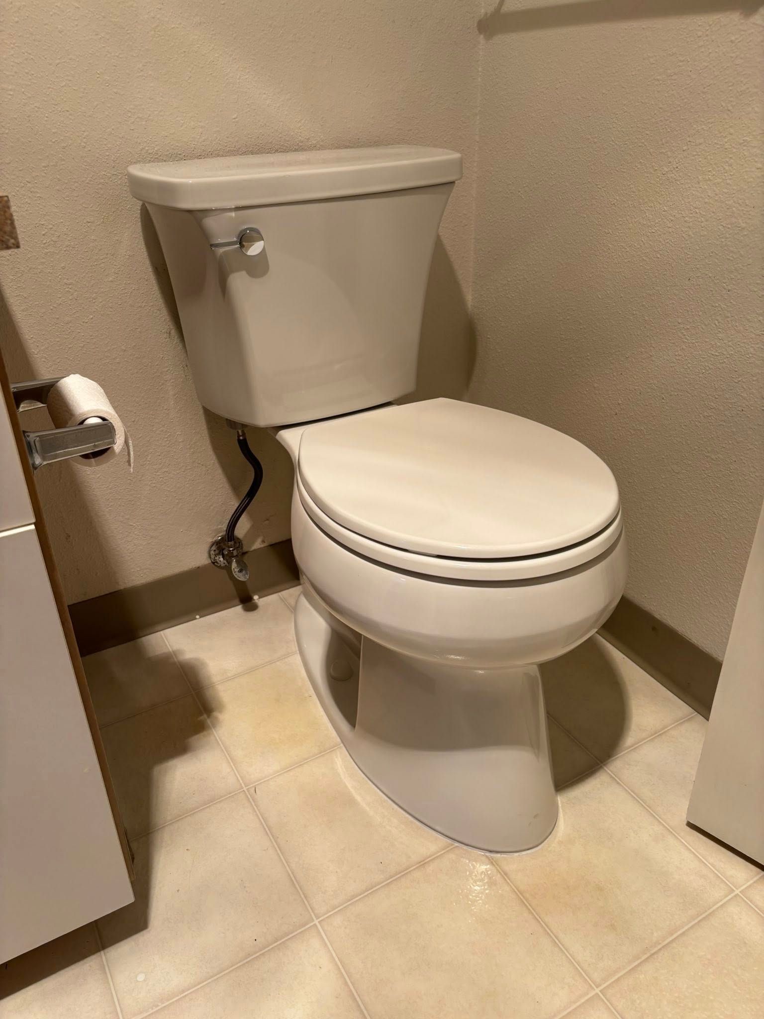 A white toilet in a bathroom with beige tile flooring and neutral-colored walls.