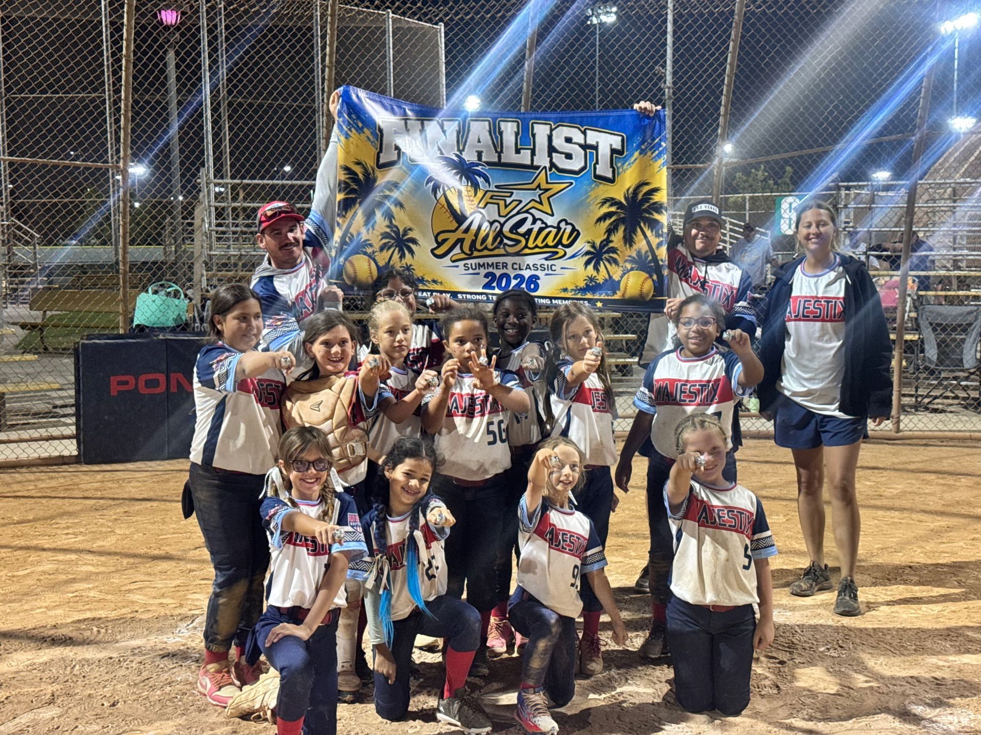 Cheer team posing on a field at night with a blue-and-yellow championship banner behind them