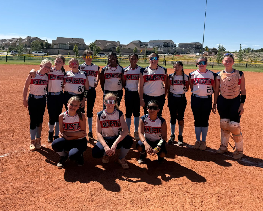 Softball team posing on a red dirt field under a clear blue sky, wearing matching jerseys.