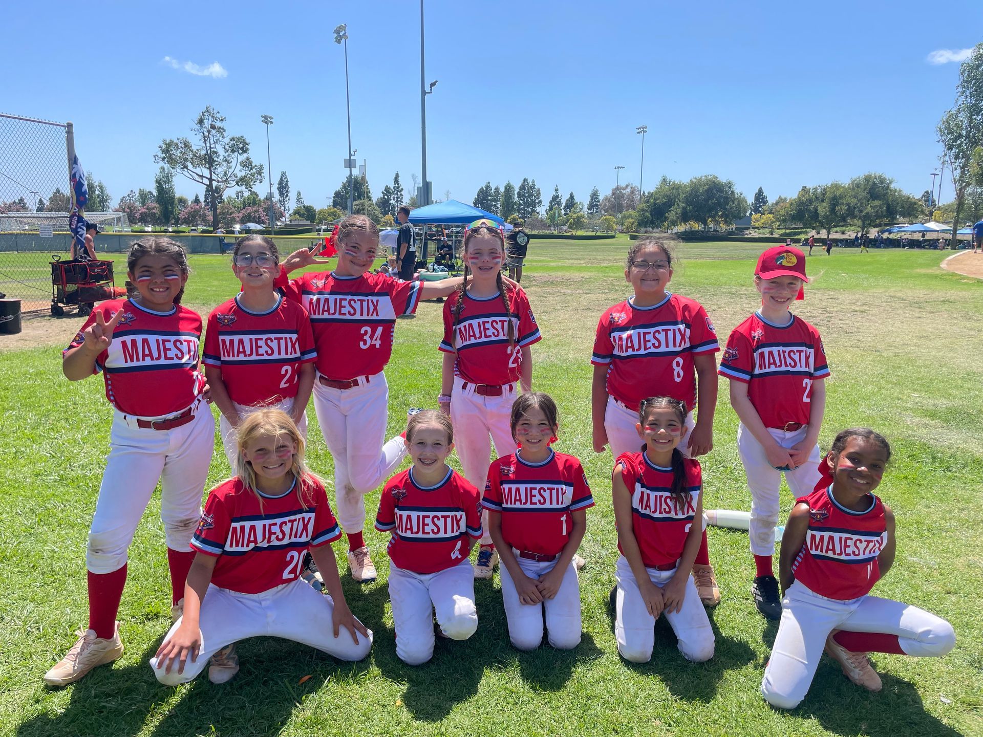 Youth baseball team in red and white uniforms posing on a grassy field under a blue sky.