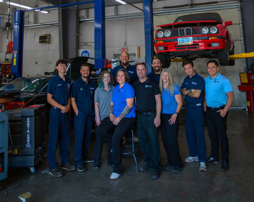 Group of auto shop employees posing in front of a red car on a lift. | Bavarian Auto Haus
