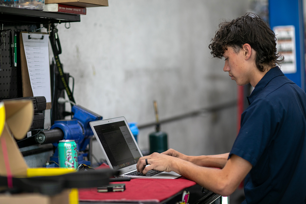 Mechanic in blue uniform types on a laptop at a workbench. | Bavarian Auto Haus