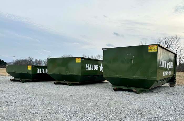Three green industrial dumpsters on a gravel lot under a cloudy sky