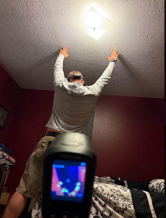 Person standing on a bed, arms raised toward a ceiling light in a red-walled bedroom.
