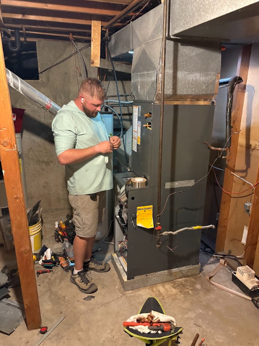 Man working on a furnace in a basement utility room with exposed ductwork