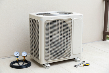 Outdoor air conditioner unit with pressure gauges and tools on the ground beside it