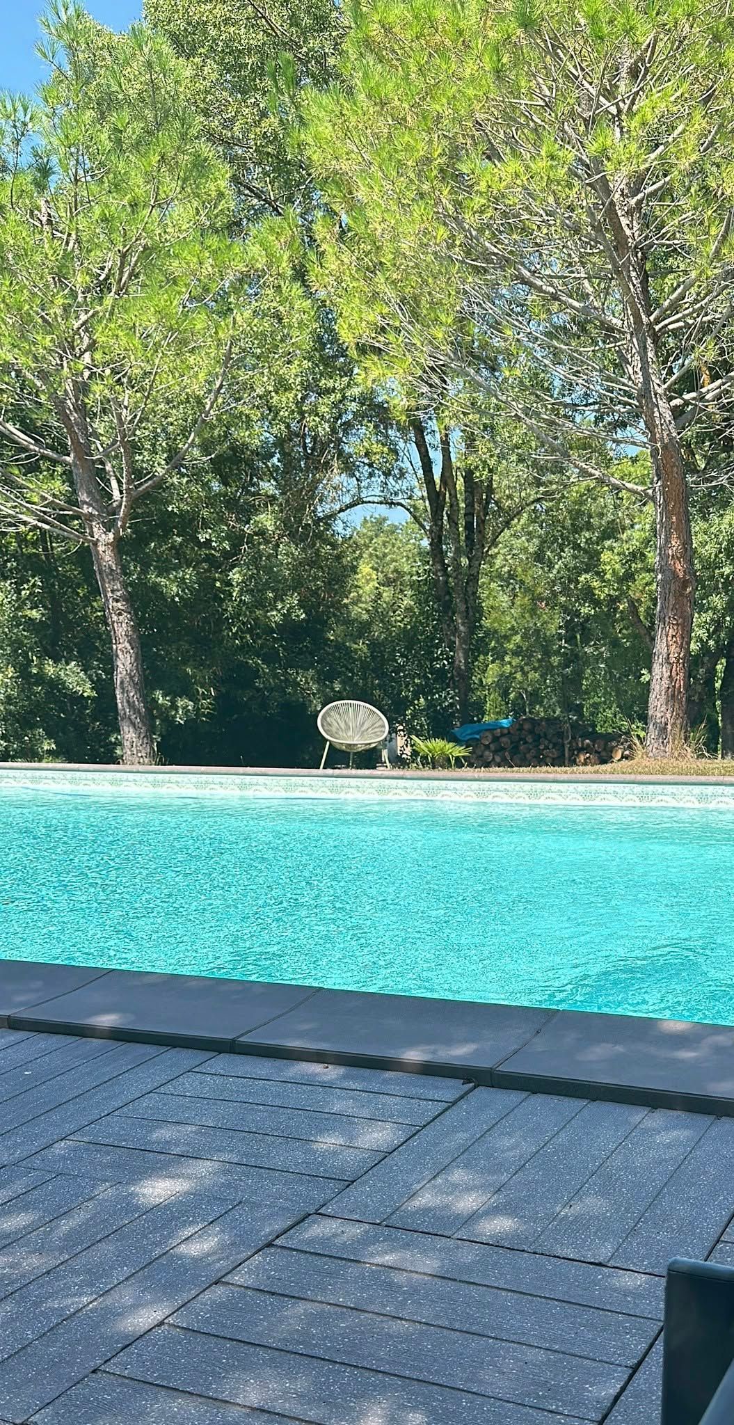 Turquoise swimming pool beside a stone deck, with tall green trees in the background.