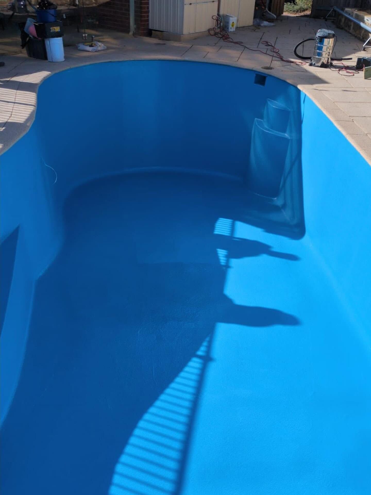Blue empty swimming pool under bright sunlight, with shadows cast across the floor.