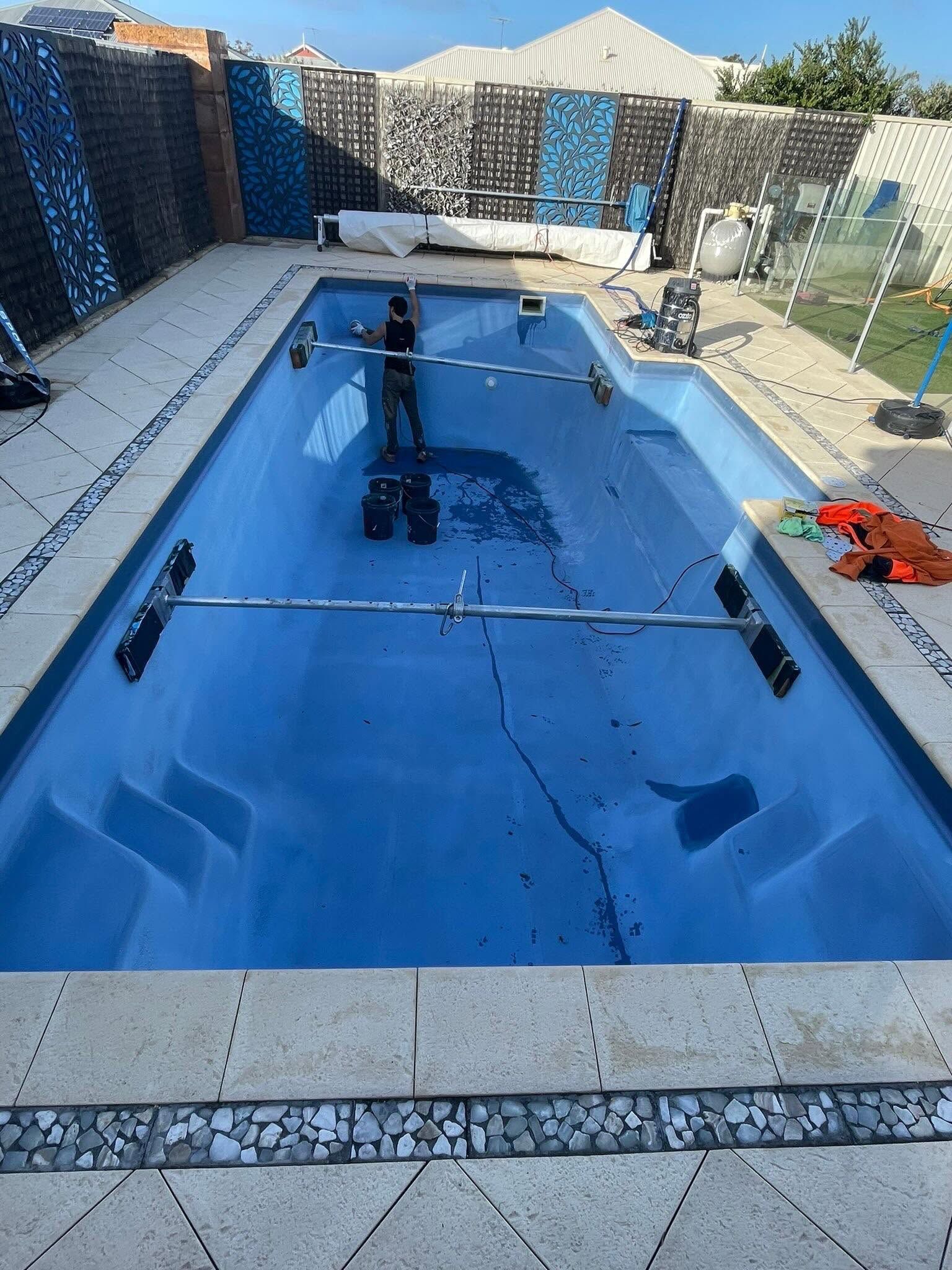 Empty backyard pool under construction, lined in bright blue with equipment and fencing around it