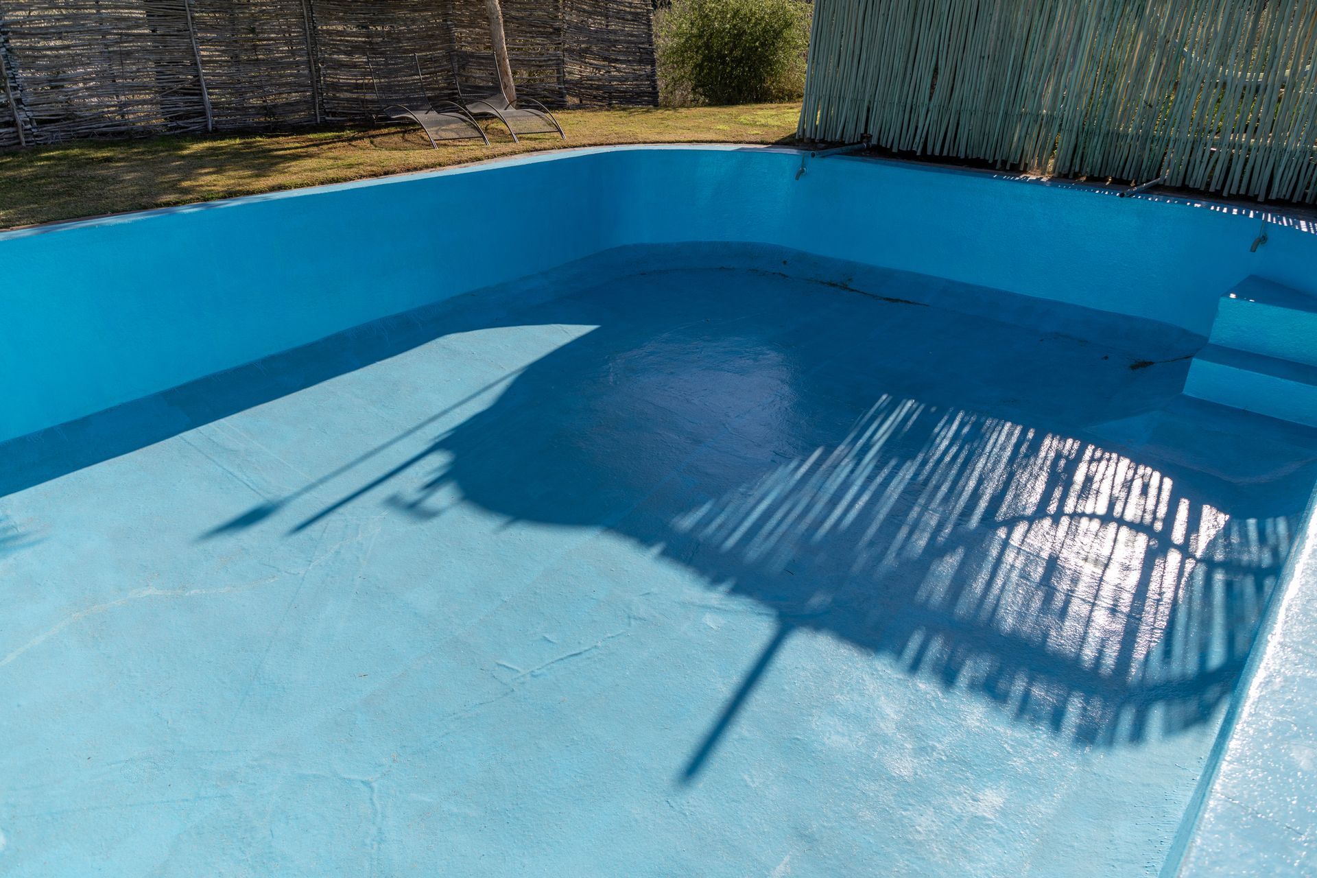Empty blue swimming pool with sunlight reflections and shadows on the water surface