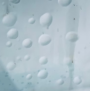 Water droplets on a pale blue glass surface, with blurred shapes behind it